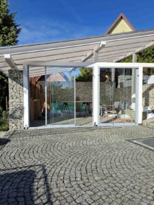 Szklane szyby przesuwne zamontowane w białym drewnianym zadaszeniu tarasu