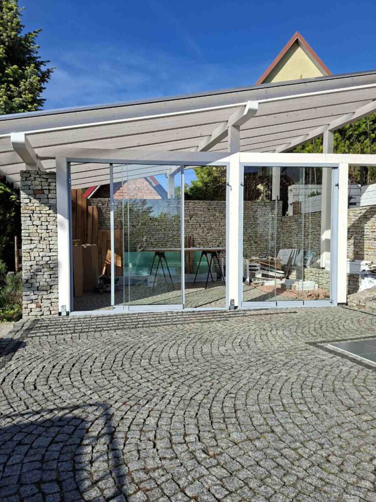 Szklane szyby przesuwne zamontowane w białym drewnianym zadaszeniu tarasu