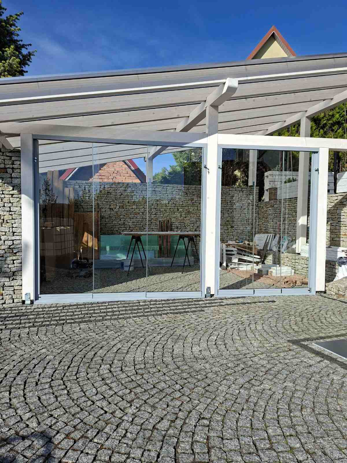 Szklane ściany przesuwne zamontowane w białym drewnianym zadaszeniu tarasu