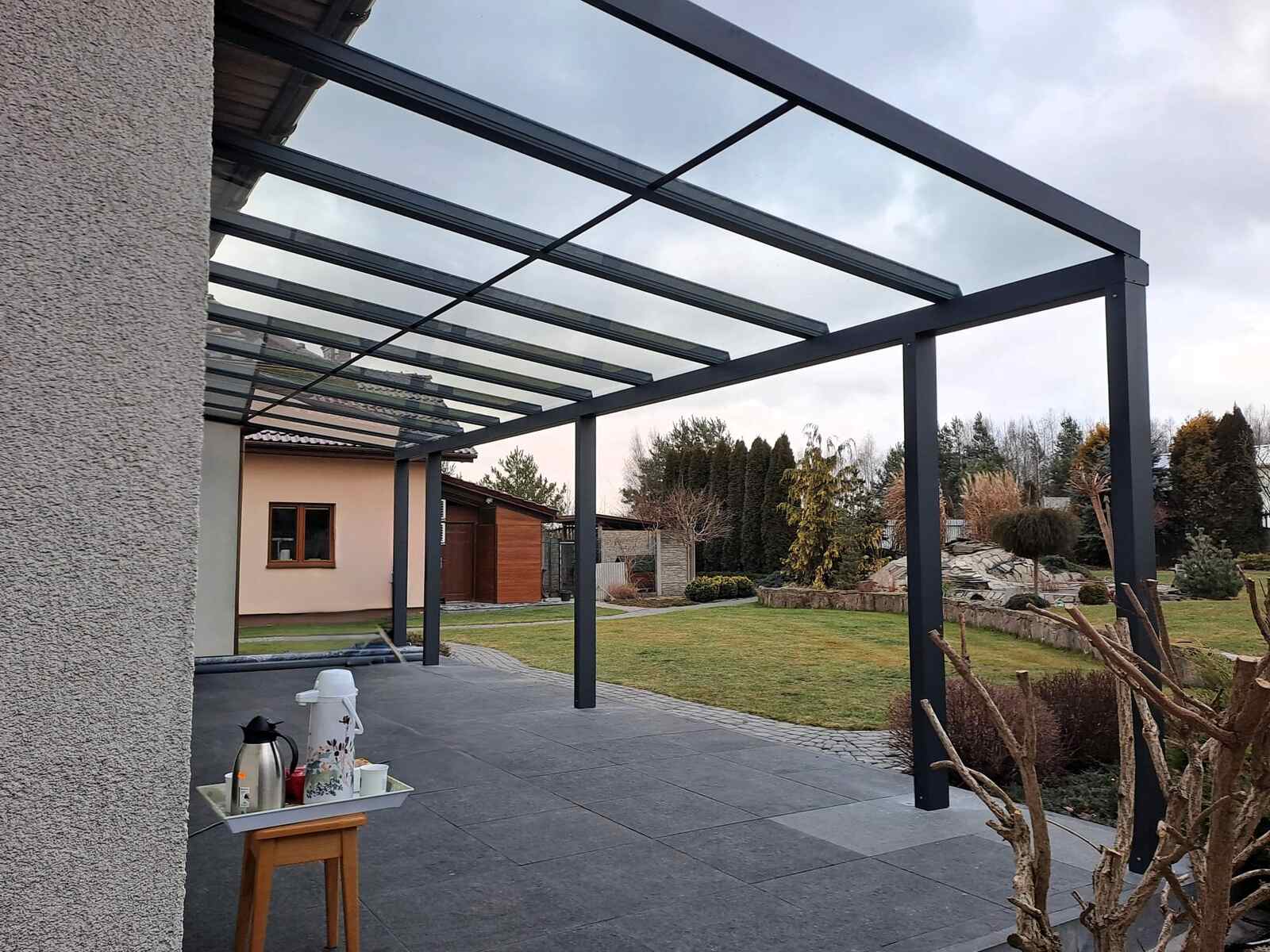 Szklane zadaszenie tarasu z widokiem na ogród i naturalną przestrzeń zieloną