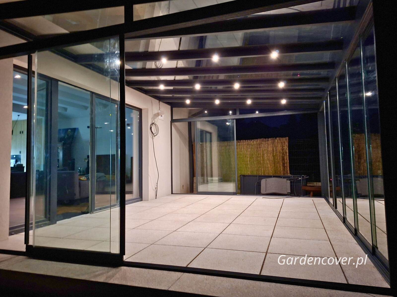 Przeszklona zabudowa tarasu w Poznaniu z oświetleniem wieczornym przy domu jednorodzinnym